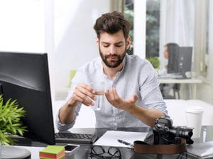 Bearded man at computer taking pills may need benzo addiction treatment.