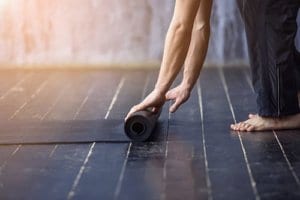 A closeup of a man rolling up a yoga mat after a yoga therapy session