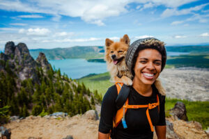 a person hikes near a lake with a dog on their back after completing a sober living program