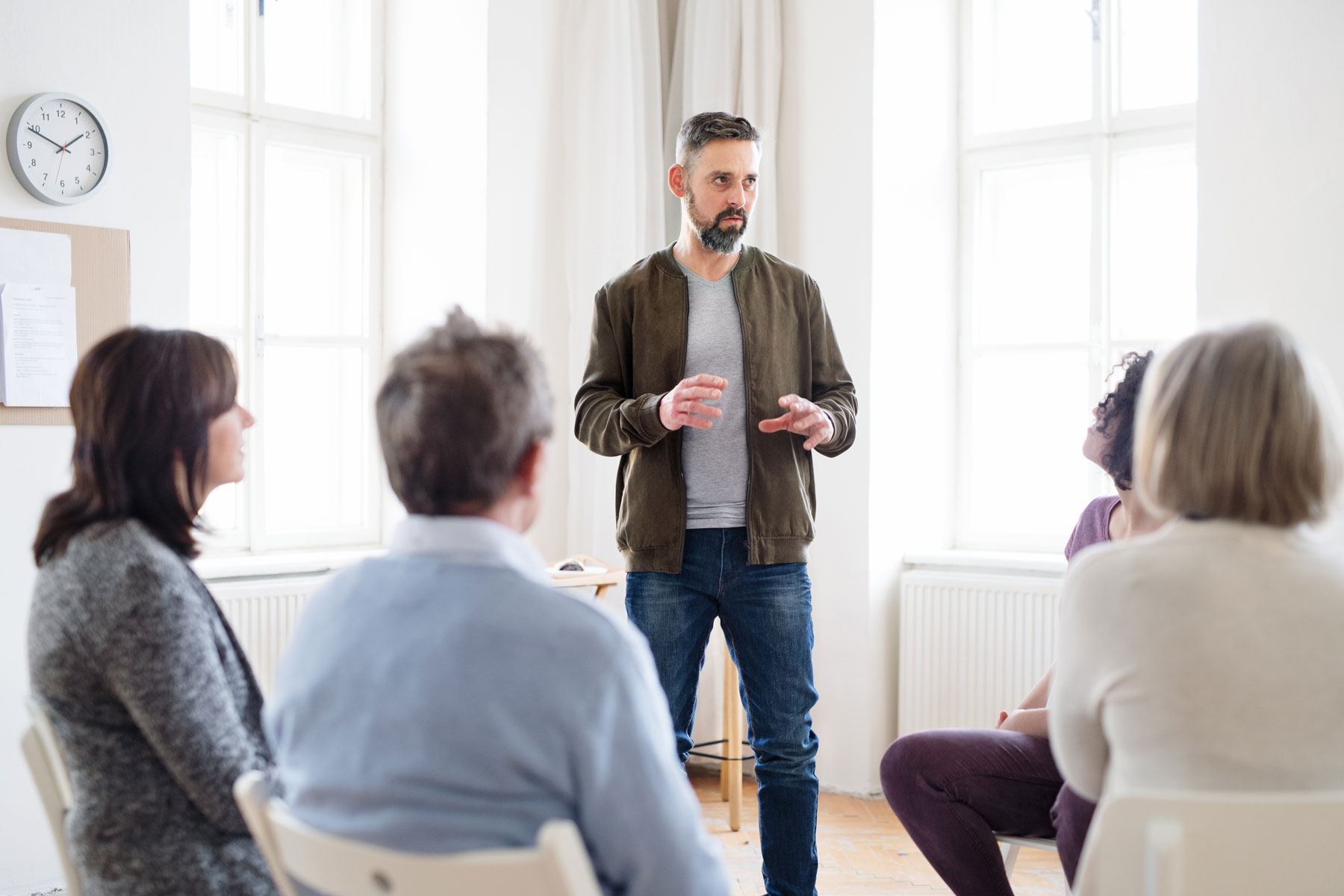 man standing to address members of a group therapy session as part of bipolar disorder treatment.