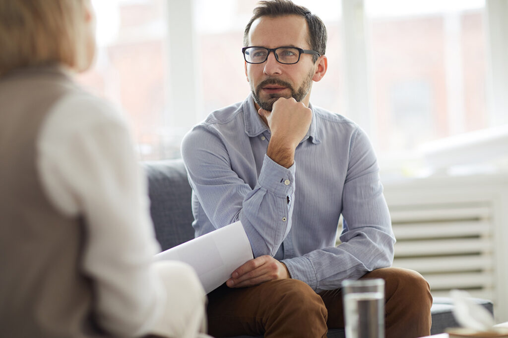 pondering man with glasses sits while listening to his therapist in his cocaine addiction treatment