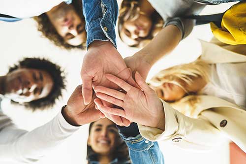 image of five people putting their hands together in a circle preparing to celebrate group therapy for addiction treatment
