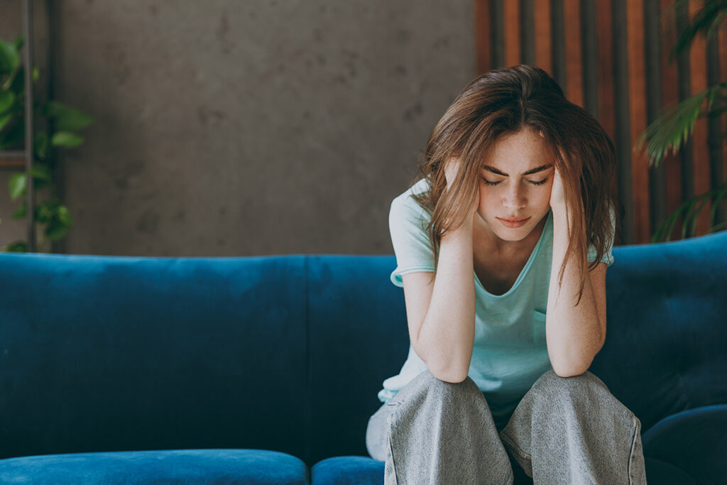an upset woman holds the side of her head while also sitting on a couch