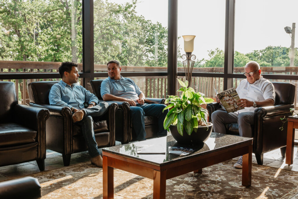a group of men reading alumni newsletters and chatting
