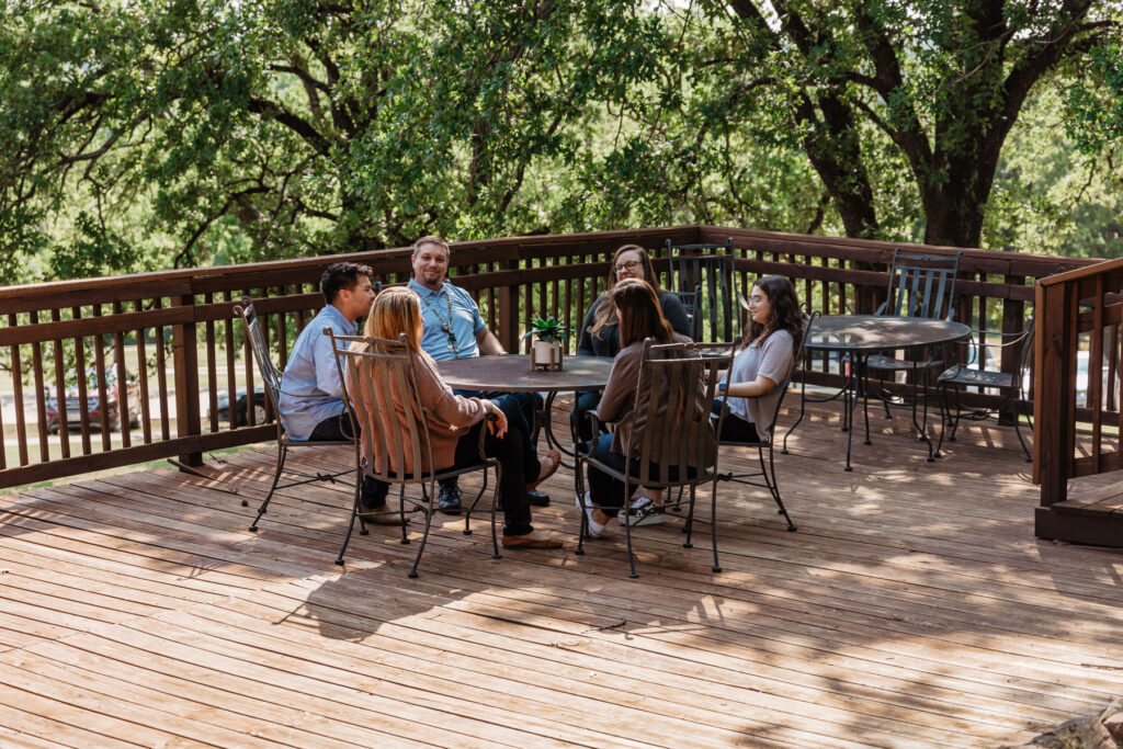 group of men and women seated outdoors on a patio overlooking scenic grounds of treatment center campus