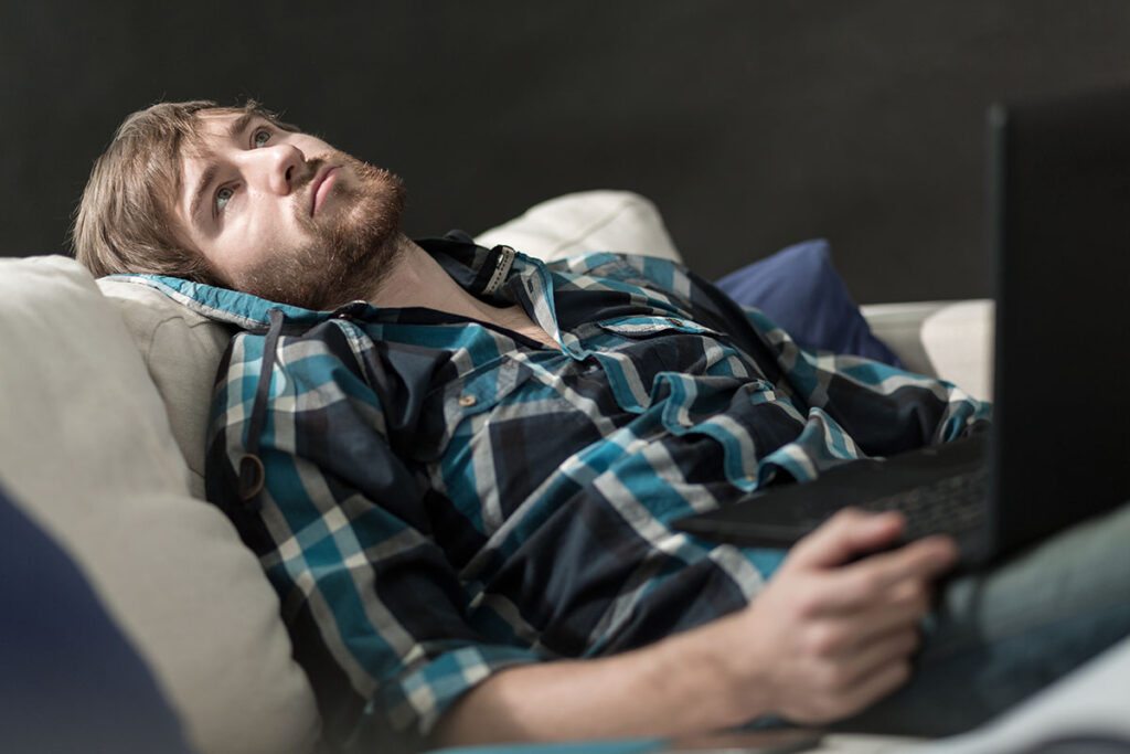 young man with haunted expression laying on couch with phone in his hand wondering what is compulsive masturbation disorder?