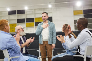 young man standing up in and addressing a group as part of an aftercare program for addiction treatment.