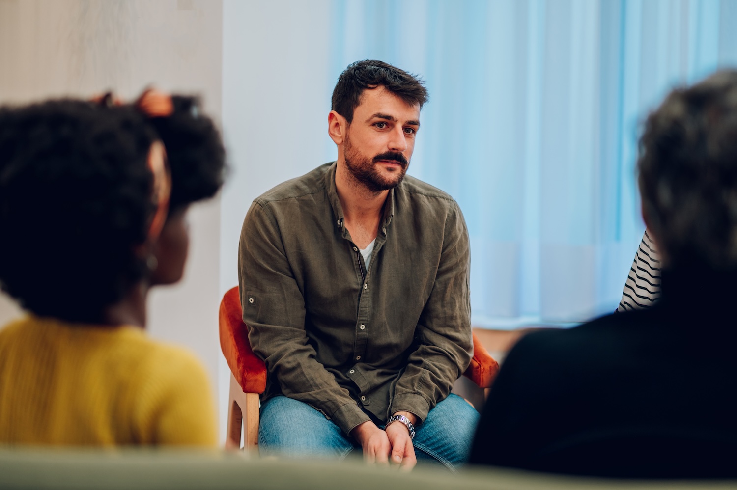 Man sitting in a group setting listens attentively during a discussion, appearing thoughtful and engaged.