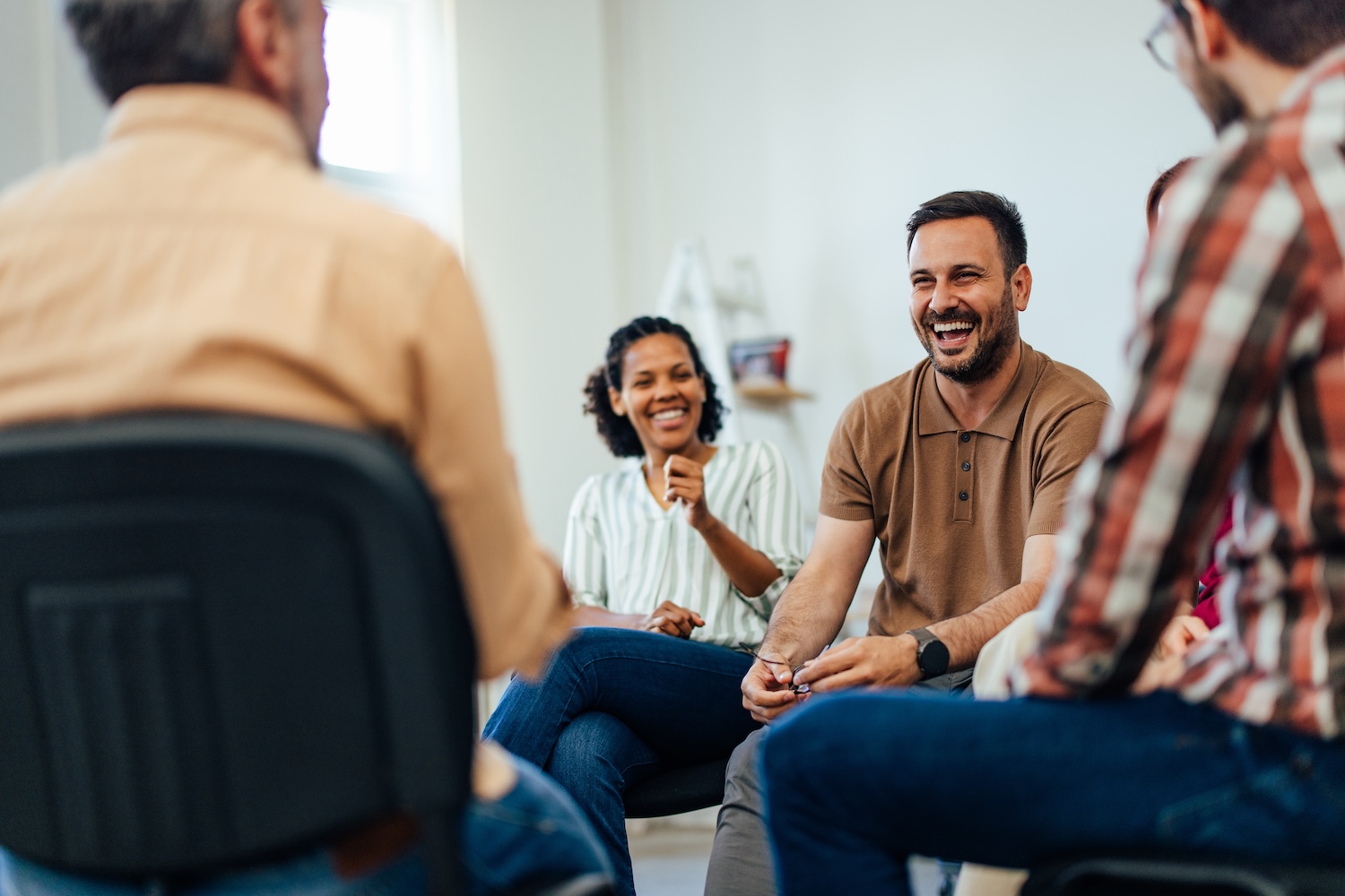 A group of adults sitting in a circle during a support group session, laughing and smiling as they talk together.